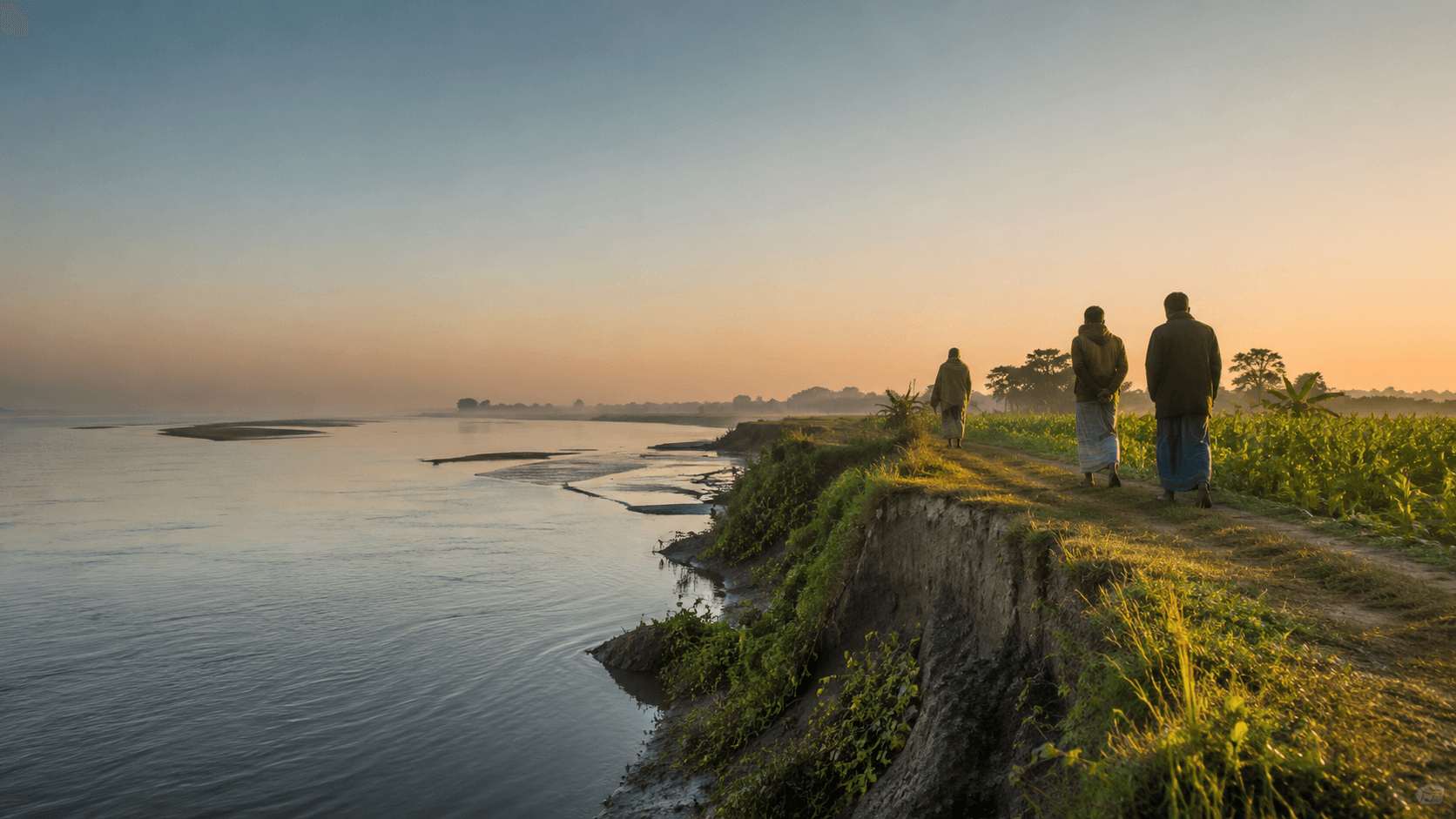 People walking beside cultivated land on an eroding riverbank in Bangladesh at dawn